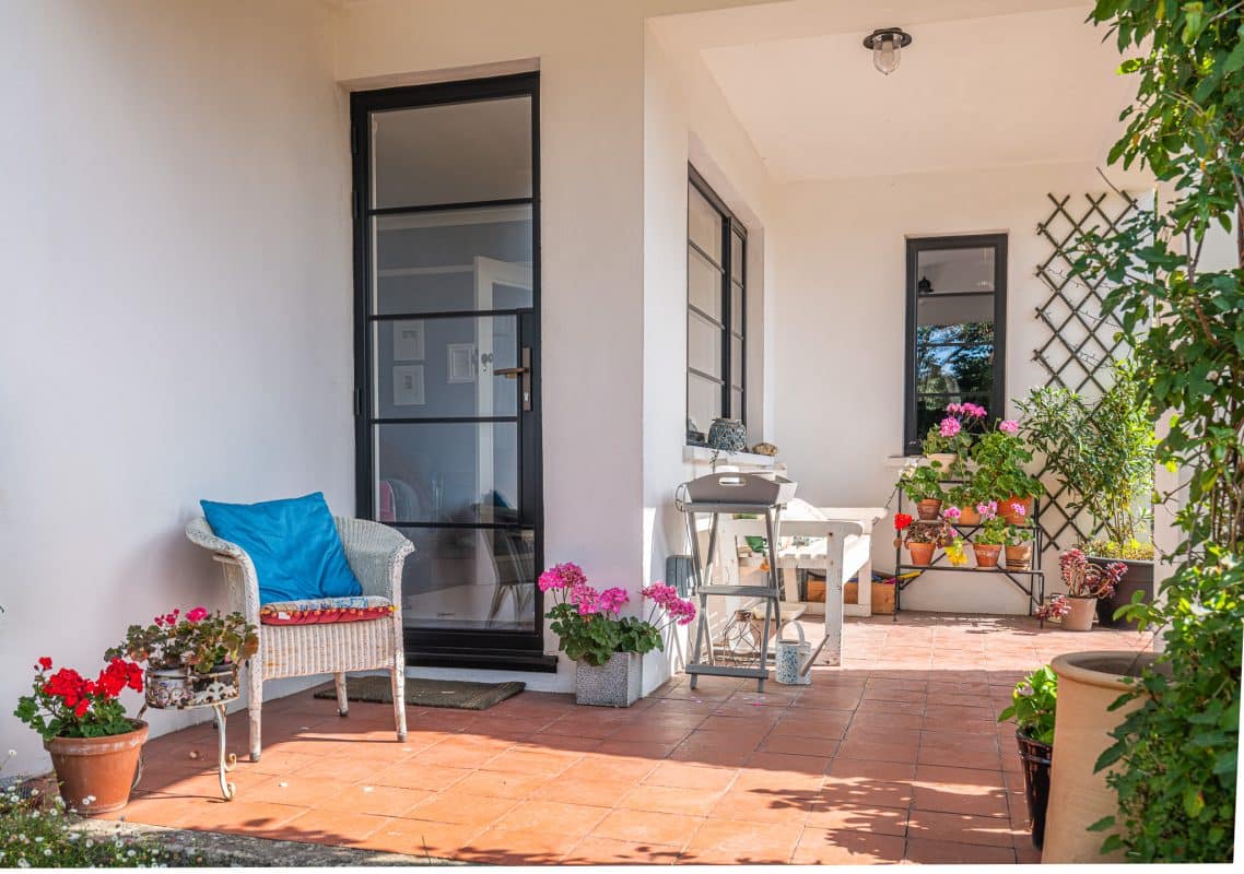 steel look windows and doors in bath house showing tasteful porch area with wicker chairs, bench and plant pots