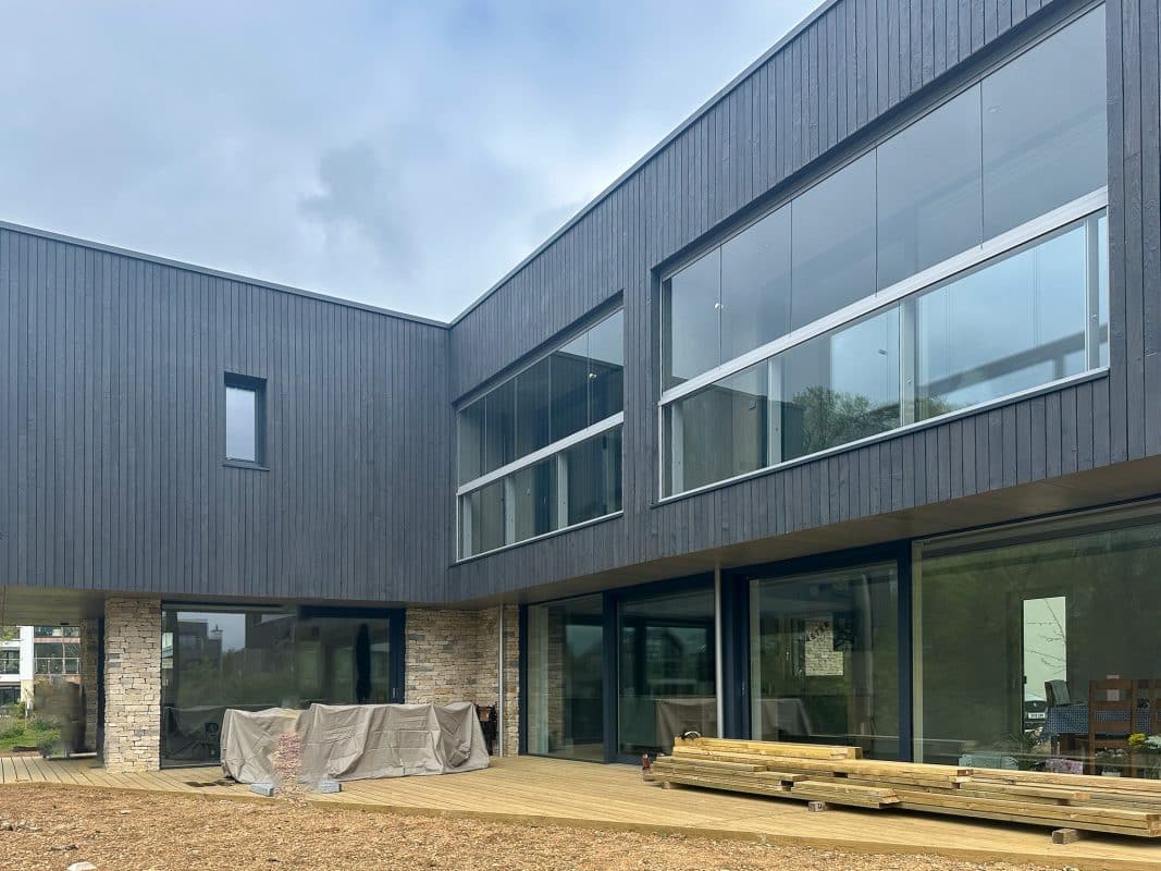 Timber-clad house with sliding doors on the ground floor and glass balustrades to balconies above. 