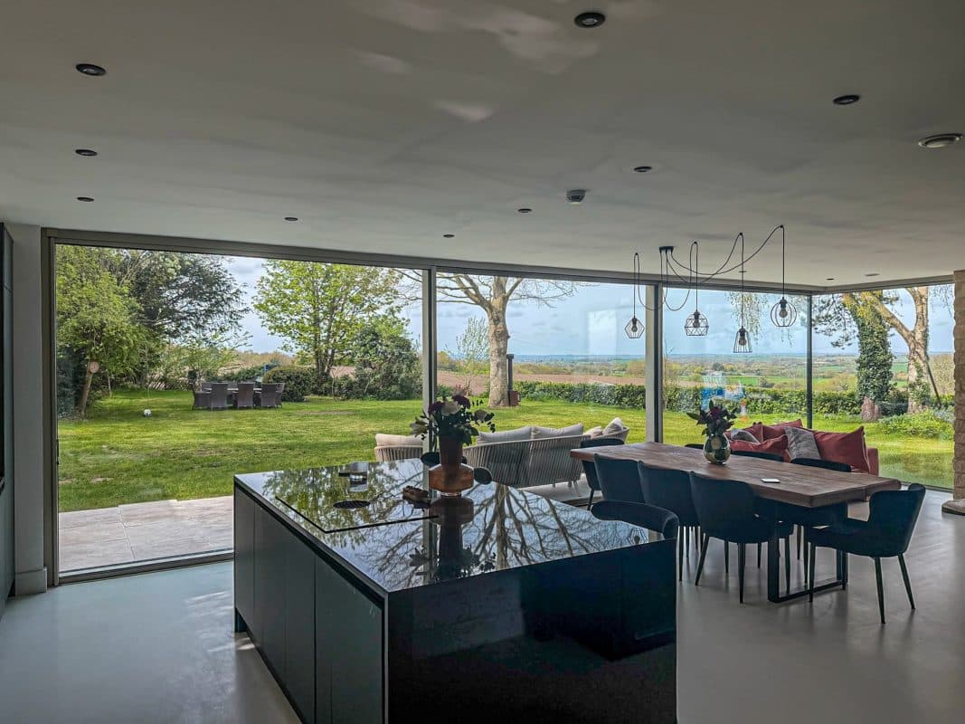 Solarlux Cero Corner Sliding Doors in a Contemporary New Build 3 inside view of grey solarlux cero corner sliding doors in contemporary kitchen with island and stylish dining table